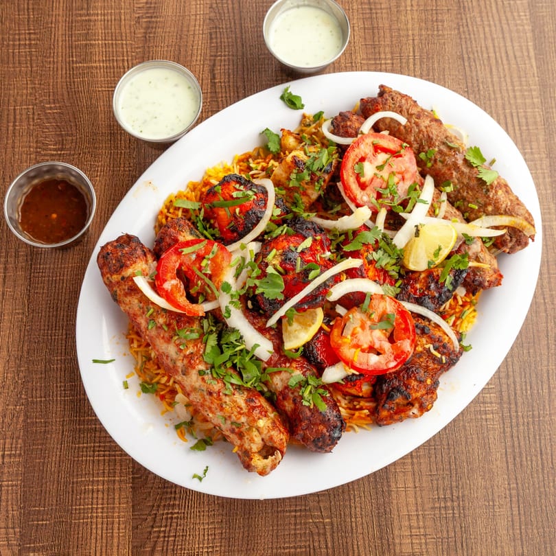 A large platter of Lahori Kabab Halal's Pakistani grilled meats, rice, tomatoes, onions, and sauces.
