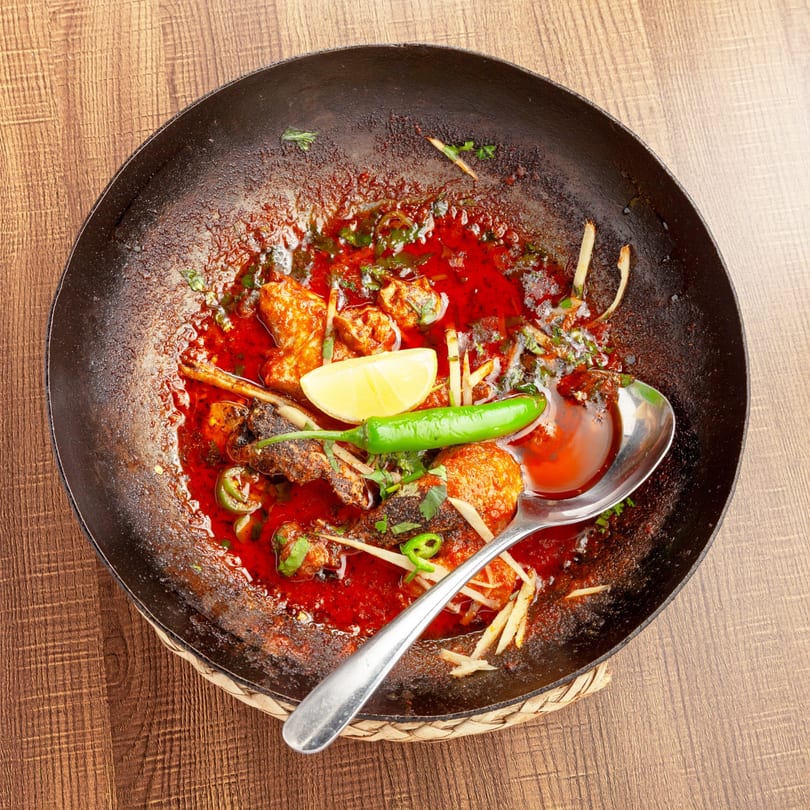 Lahori Kabab Halal's karahi dish with chicken, red sauce, lemon, and green chili in a black pan.