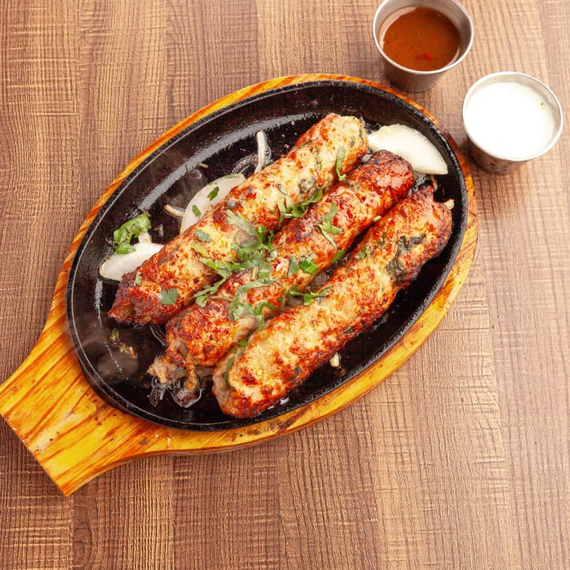 Four sizzling Lahori Kabab Halal seekh kababs on a hot plate with onions and sauces.