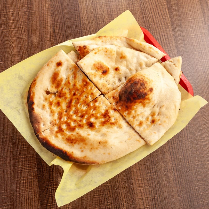 Pakistani naan bread, cut into triangles, served in a red basket lined with yellow paper.