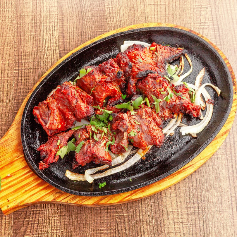 Lahori Kabab Halal's red marinated kabab meat with onions and cilantro on a sizzling platter.