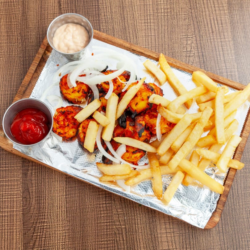 Lahori Kabab Halal's chicken tikka with fries, onions, ketchup, and sauce on foil.