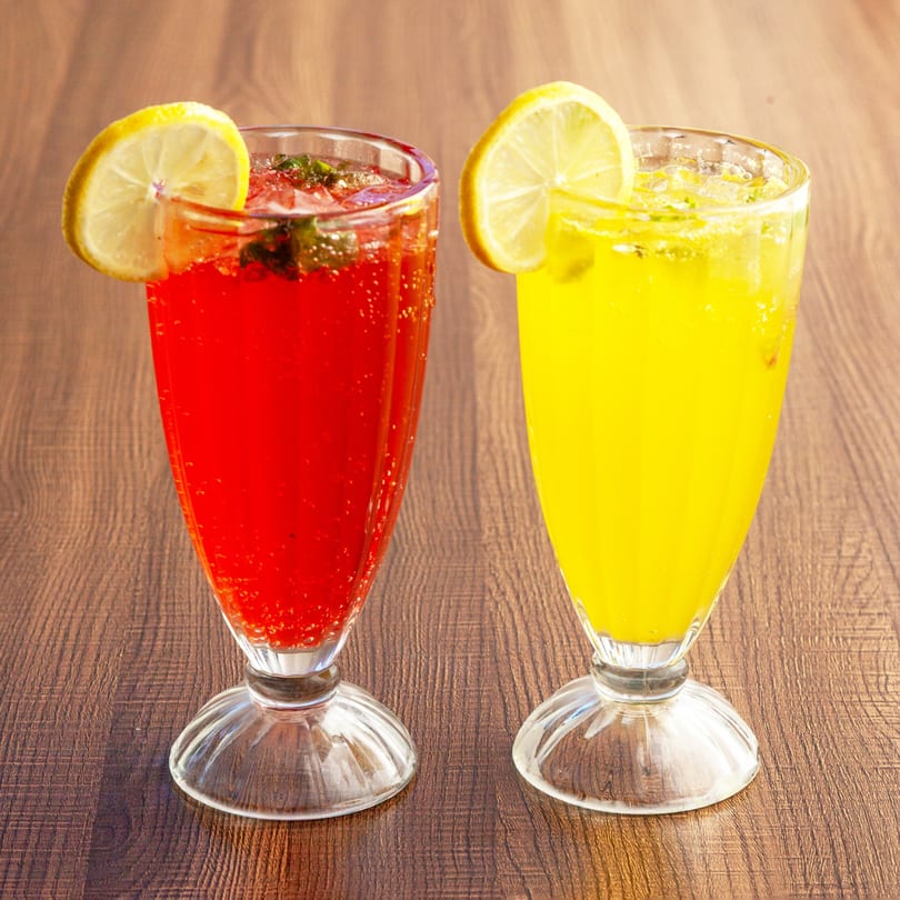 Two tall glasses of Lahori Kabab Halal's refreshing red and yellow drinks, garnished with lemon slices.